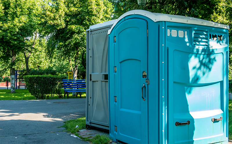 Two Joe Johnson Septic Service portable toilets in a park.